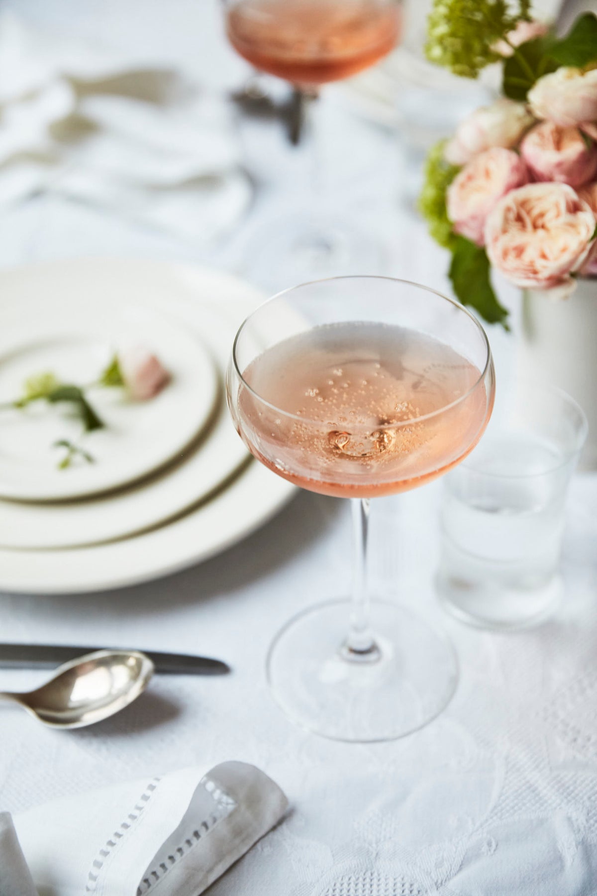 glass of rosé sparkling wine on table with roses and white crockery 