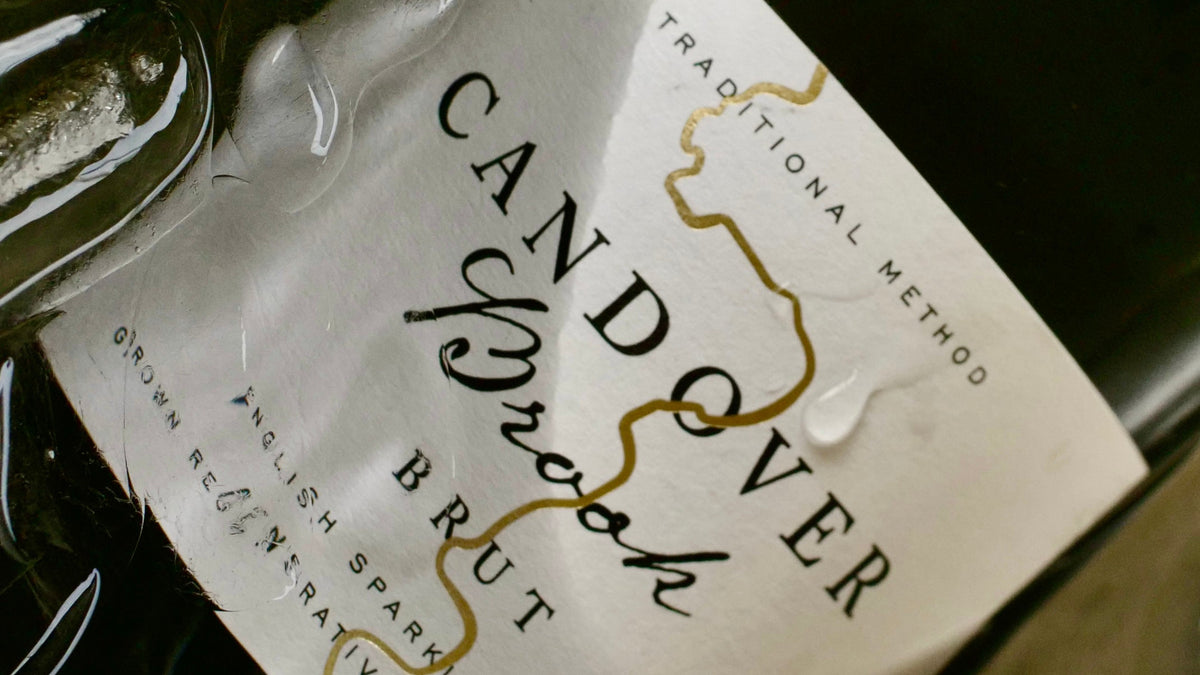 Close-up of a dark green wine bottle with a white label reading 'Candover Brook Brut' and 'Traditional Method' in elegant typography.